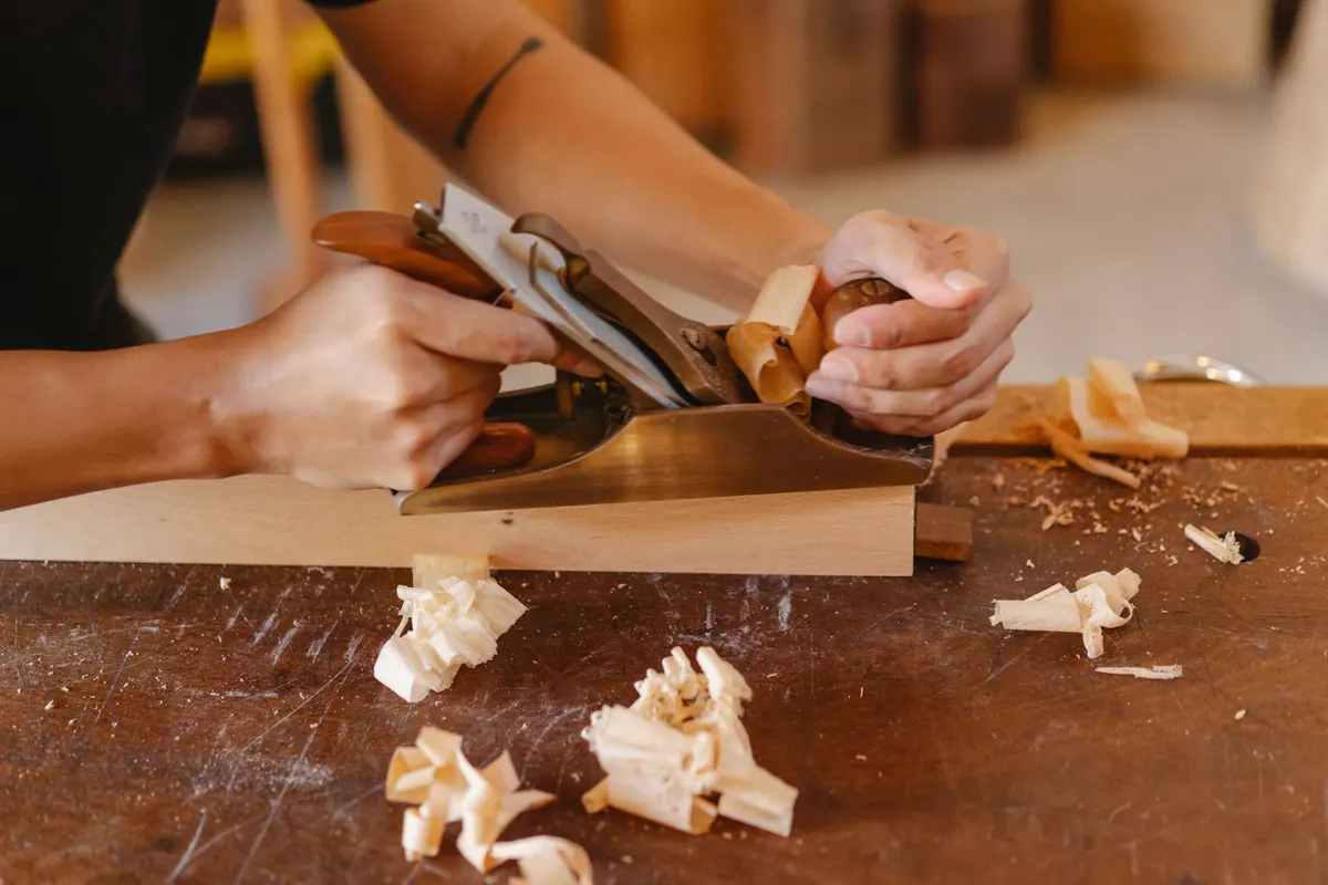 Woodworker using a hand plane on a board with shavings on the workbench