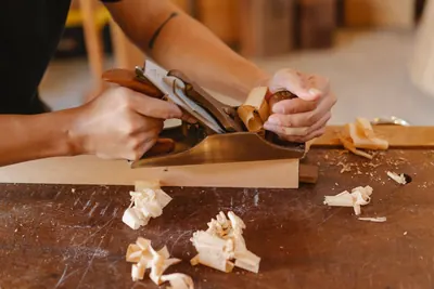 Woodworker using a hand plane on a board with shavings on the workbench