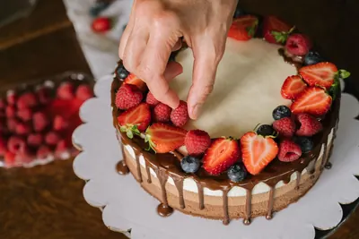 Hand decorating a chocolate drip cake with fresh strawberries