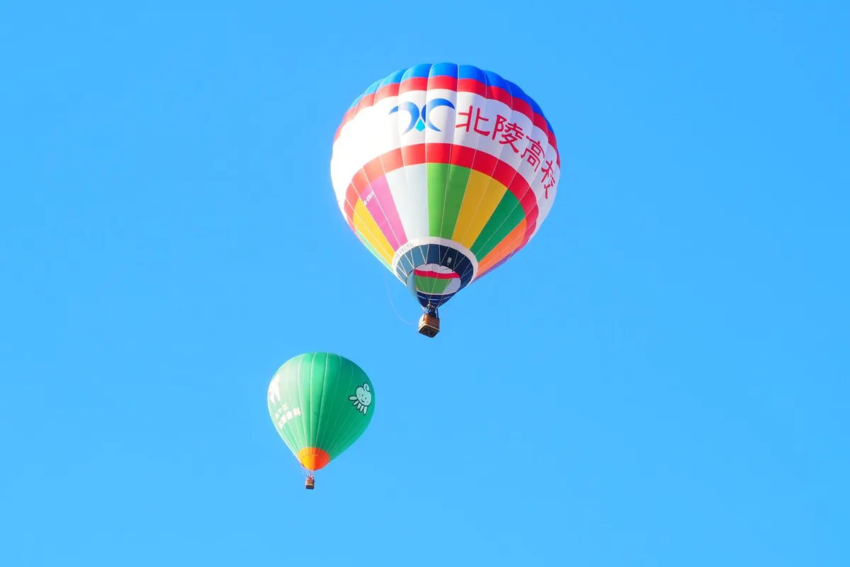Two balloons rising into a clear blue sky