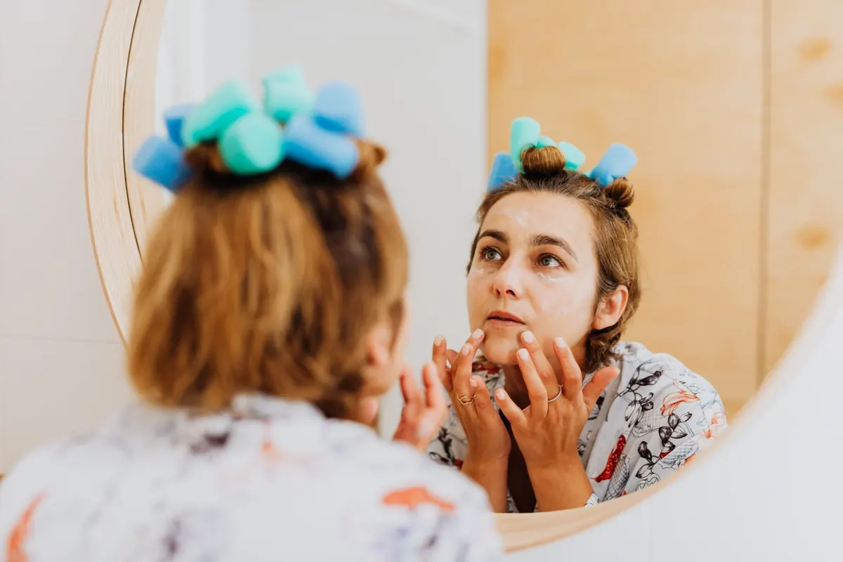 Woman applying a skincare face mask in front of a mirror