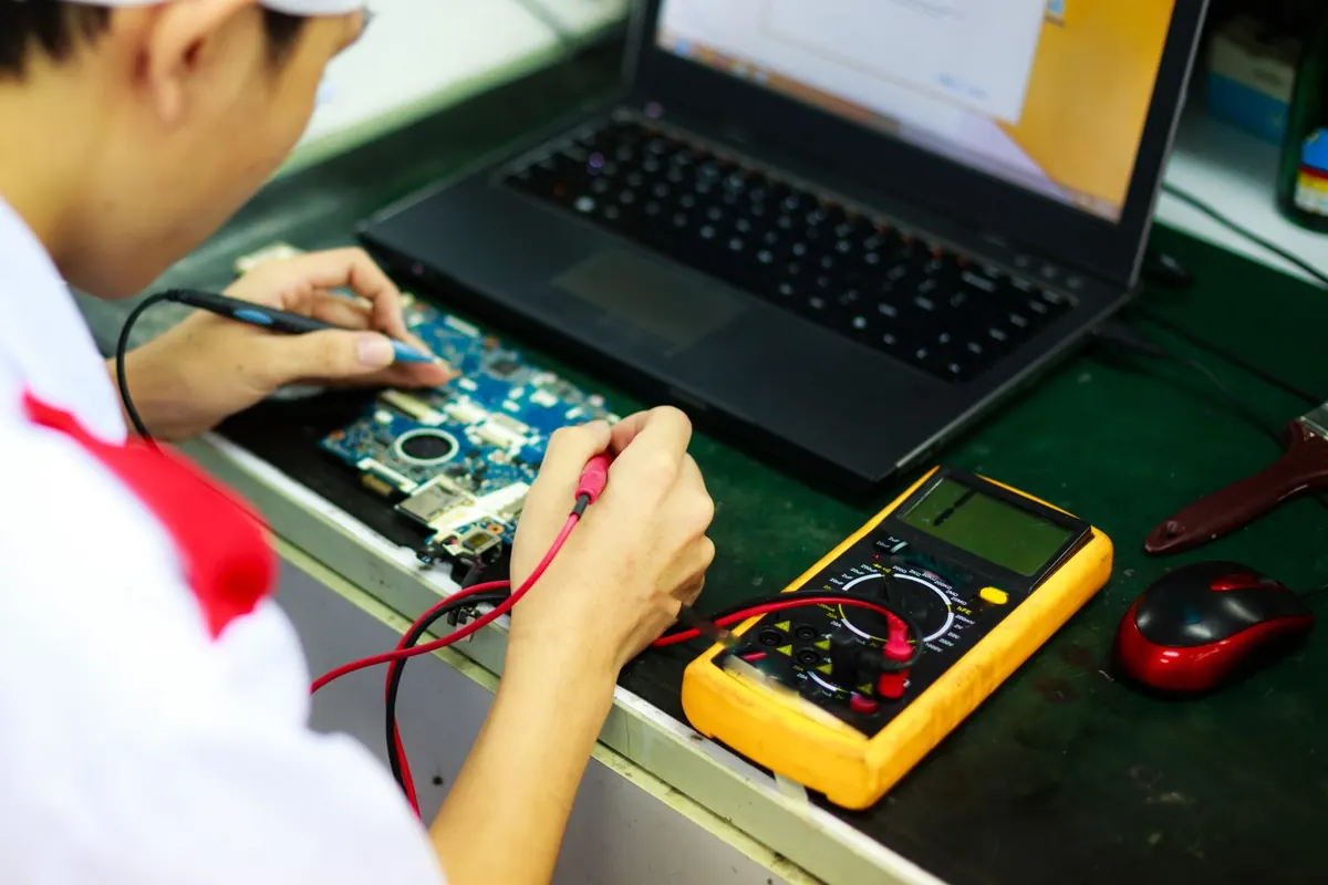Technician testing a laptop motherboard with a multimeter