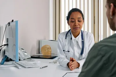 Doctor with a stethoscope listening to a patient at her desk