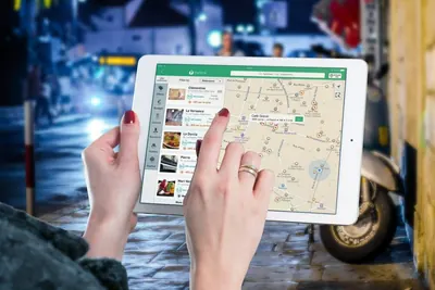 Hands using a map app on a tablet in a city street at night